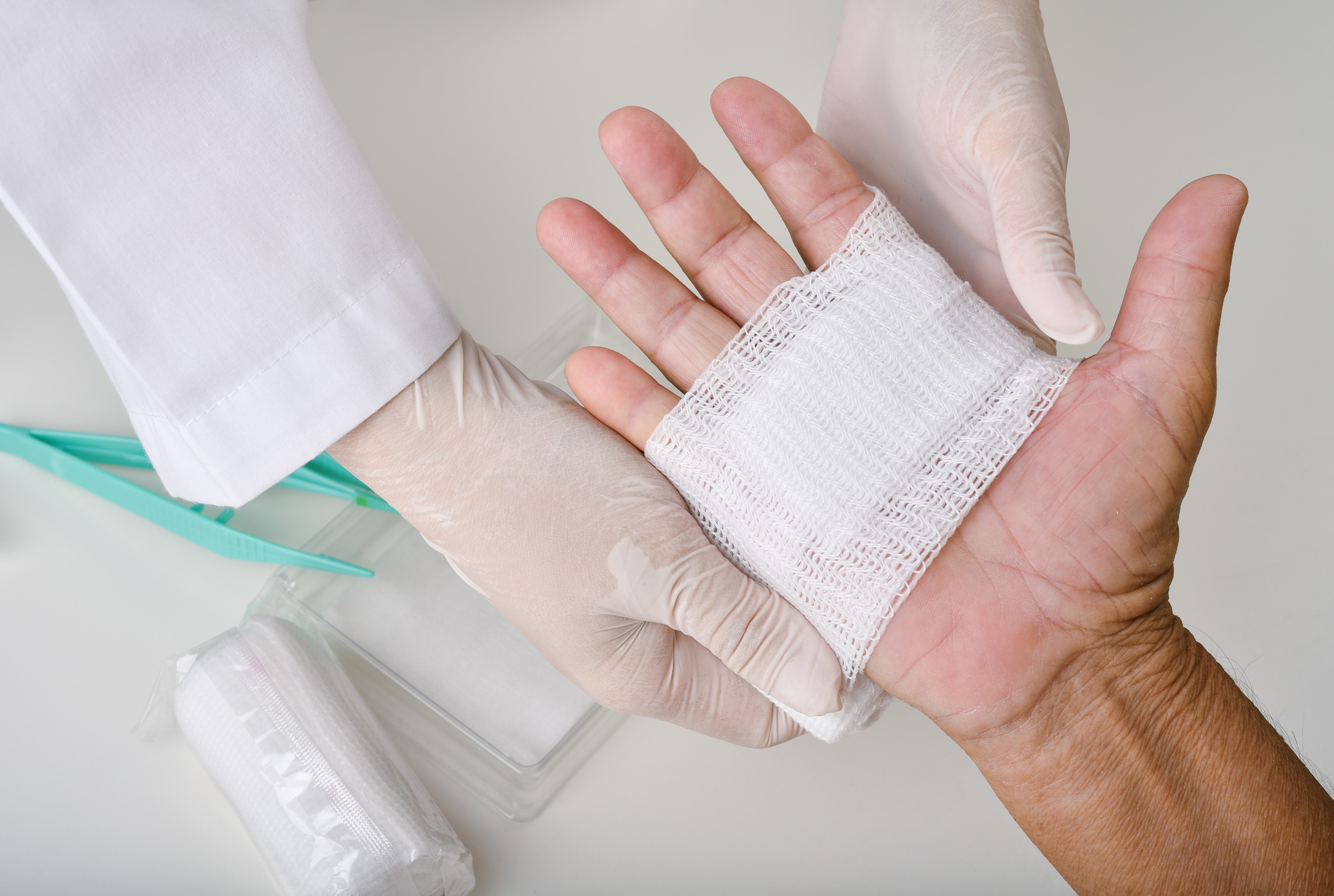 Arzt, der einen Wundverband anlegt und die Hand eines Patienten verbindet, H