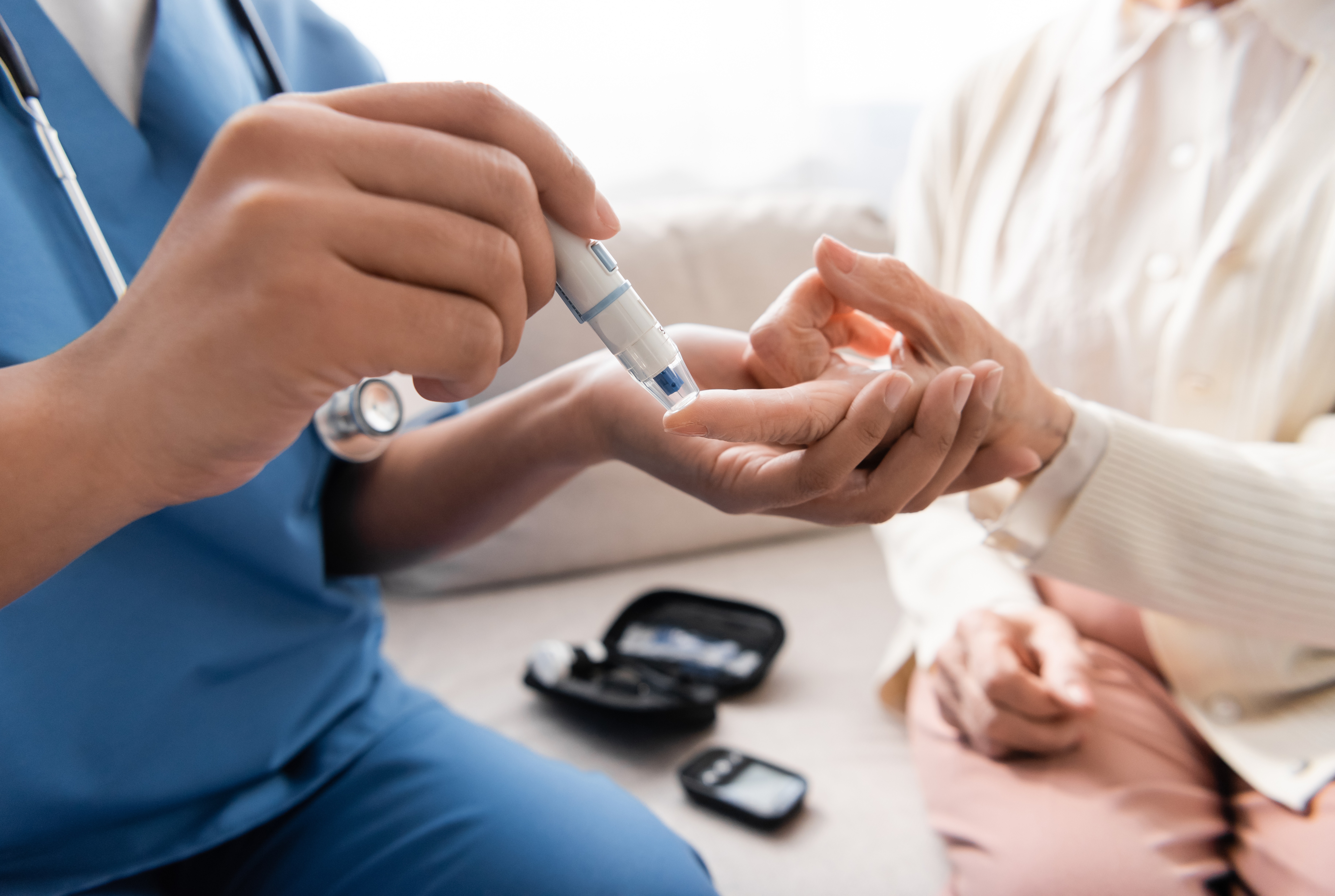 Ausschnitt einer multirassischen Krankenschwester, die einer älteren Frau mit einem Lanzettenstift eine Blutprobe entnimmt.
